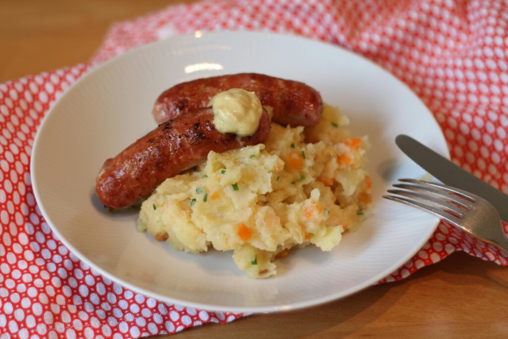 Delicious sausages with mashed potatoes and vegetables on a white plate.
